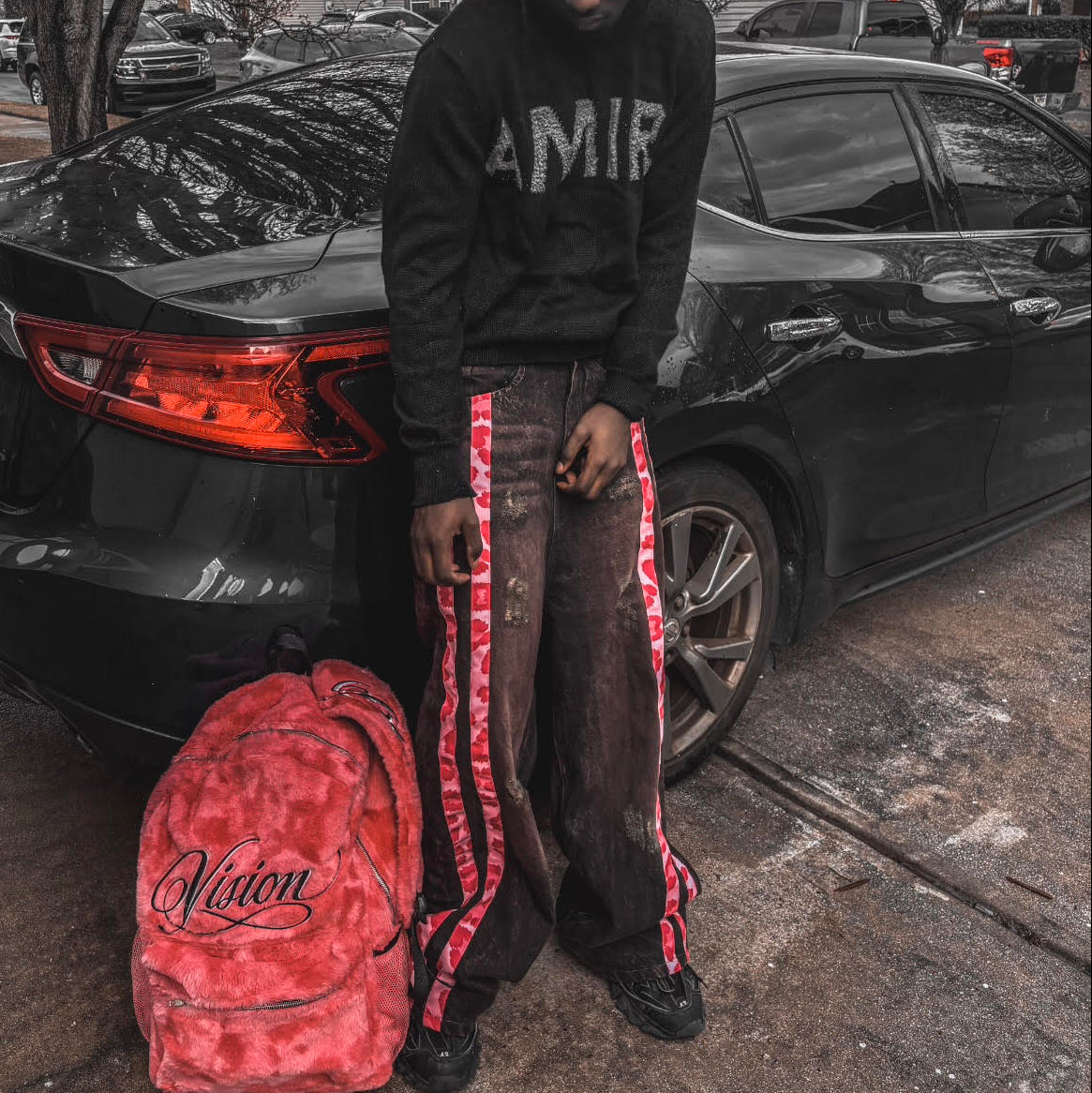 Person holding a red backpack with a visible brand logo, standing next to a black car on a street.